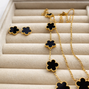 Conjunto de joyería dorado con tréboles negros: collar y aretes.