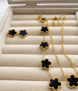 Conjunto de joyería dorado con tréboles negros: collar y aretes.